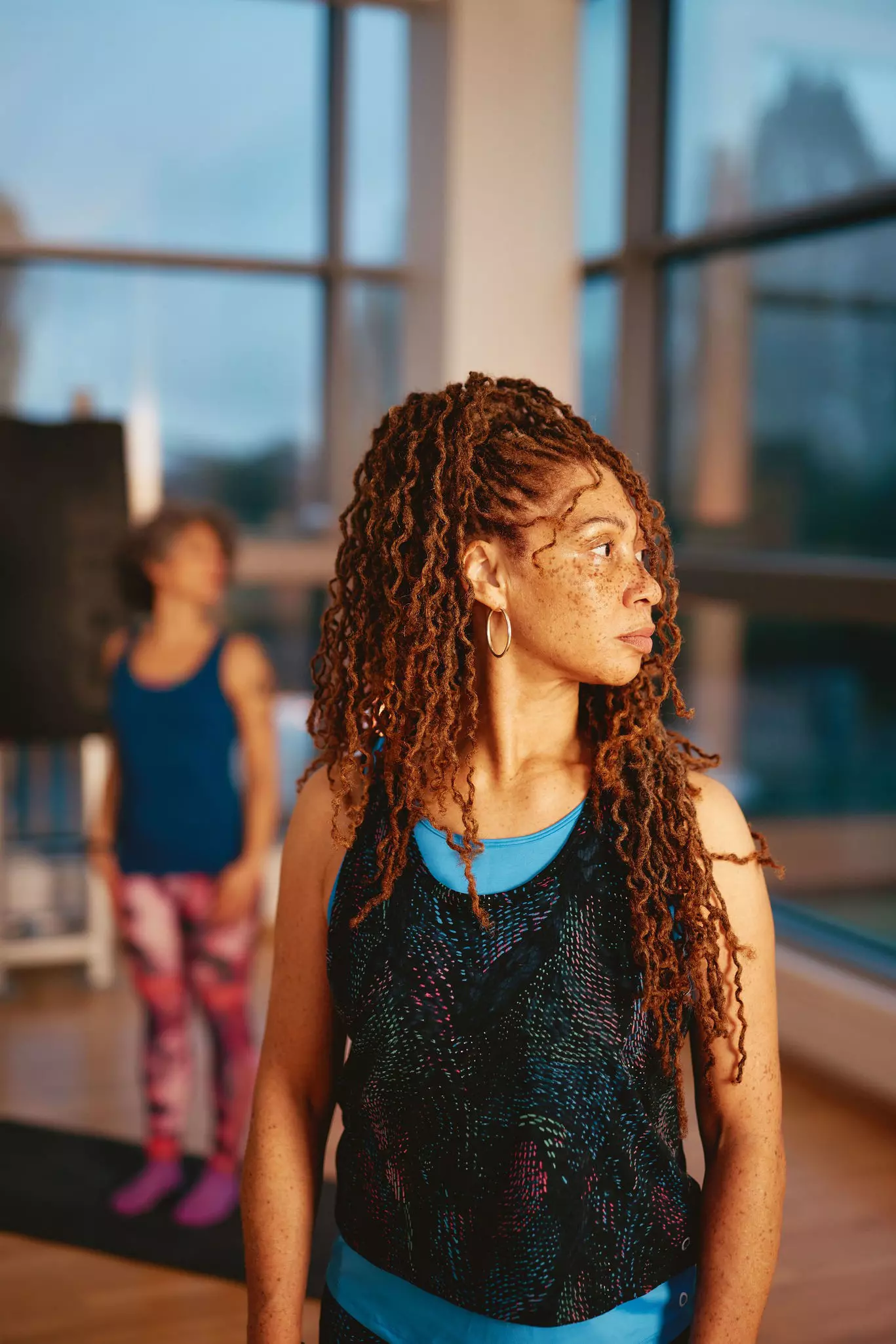 Person with long braided hair wearing a dark blue top near a bright window.