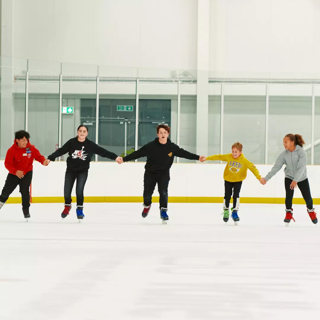 Children ice skating in a line holding hands.