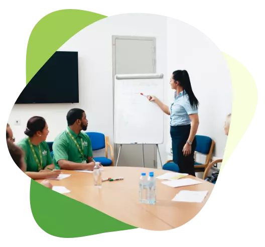 Woman leading a training session with colleagues around a table, pointing at notes on a flipchart.