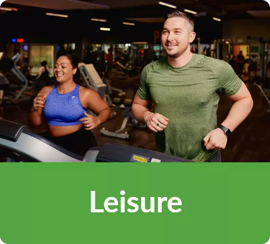 Man and woman smiling while running on treadmills in a busy gym.