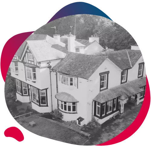 Black and white photo of a large traditional house surrounded by trees.