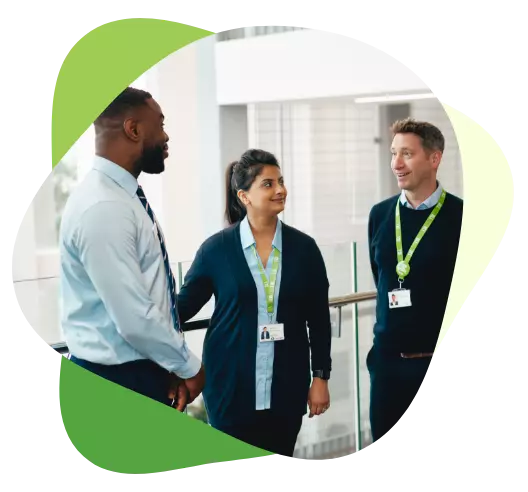 Three professionals wearing lanyards talking and smiling in a modern office setting.