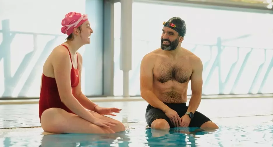 Two people chatting while sitting at the edge of a swimming pool.