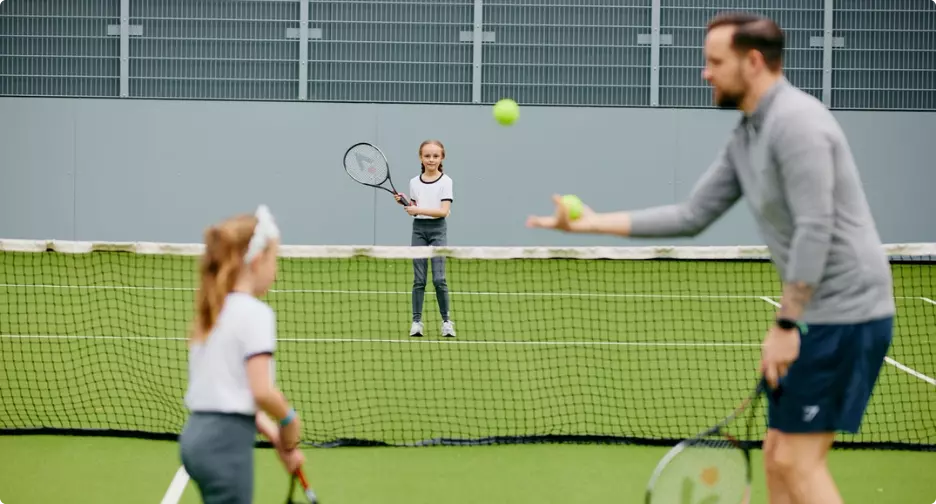 Children playing tennis with a coach on an outdoor court.