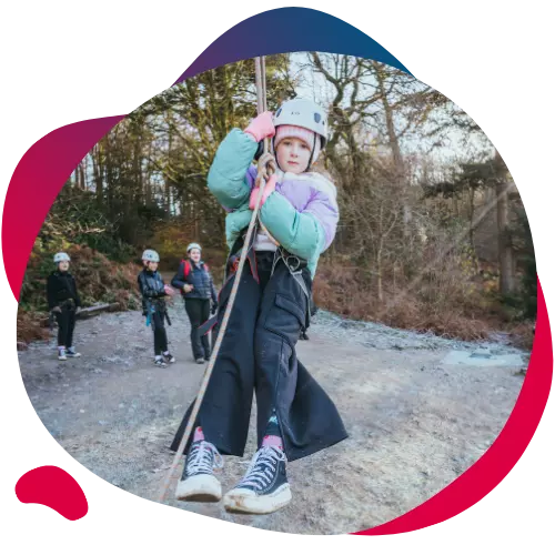 Girl in a helmet gripping a rope and swinging during an outdoor activity.