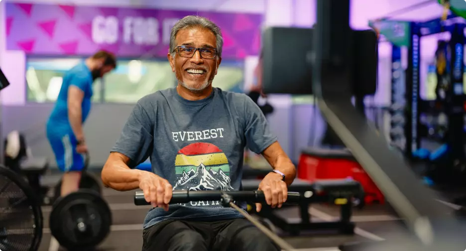 Man smiling while using a rowing machine at the gym.