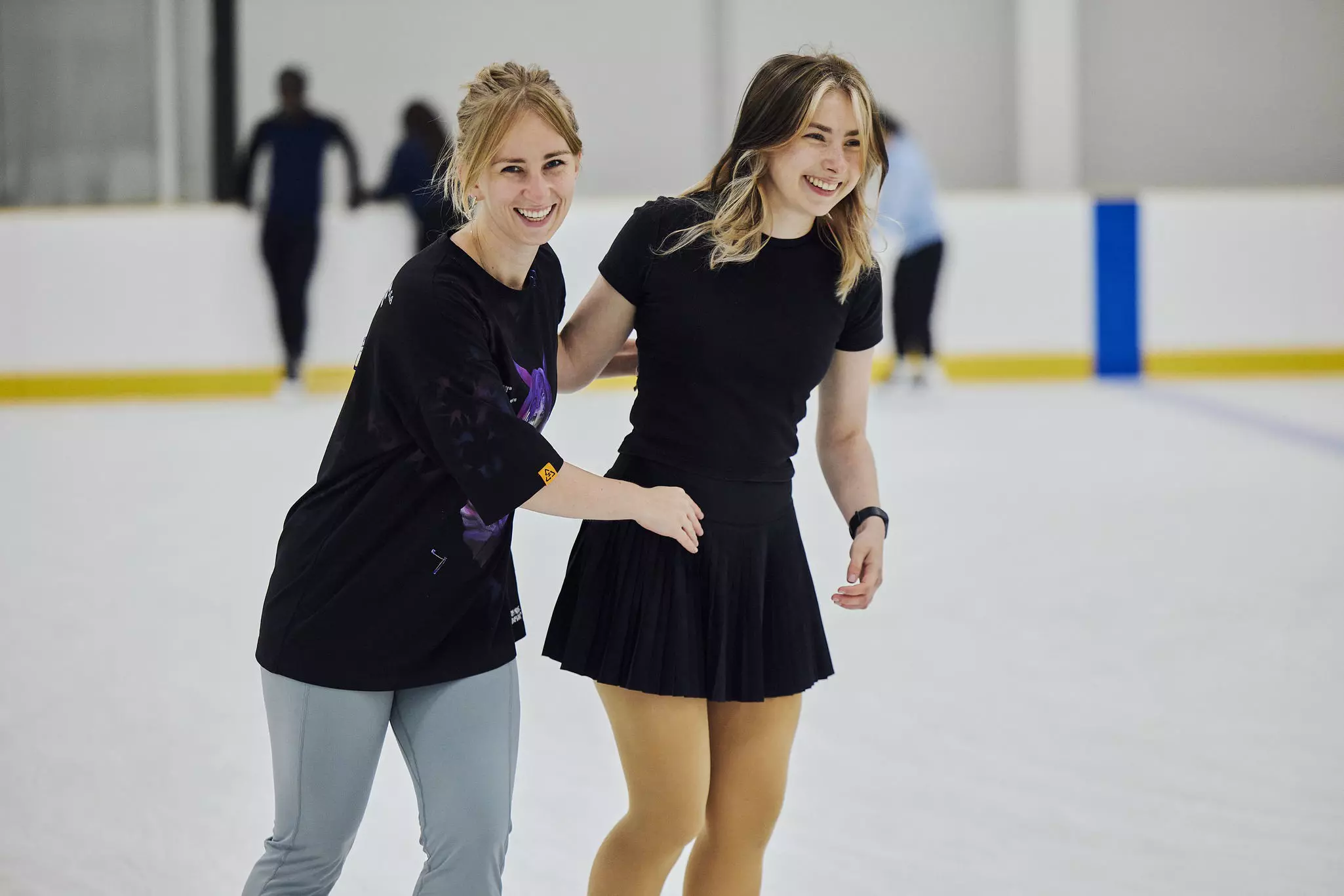 Two girls smiling while on the ice rink.