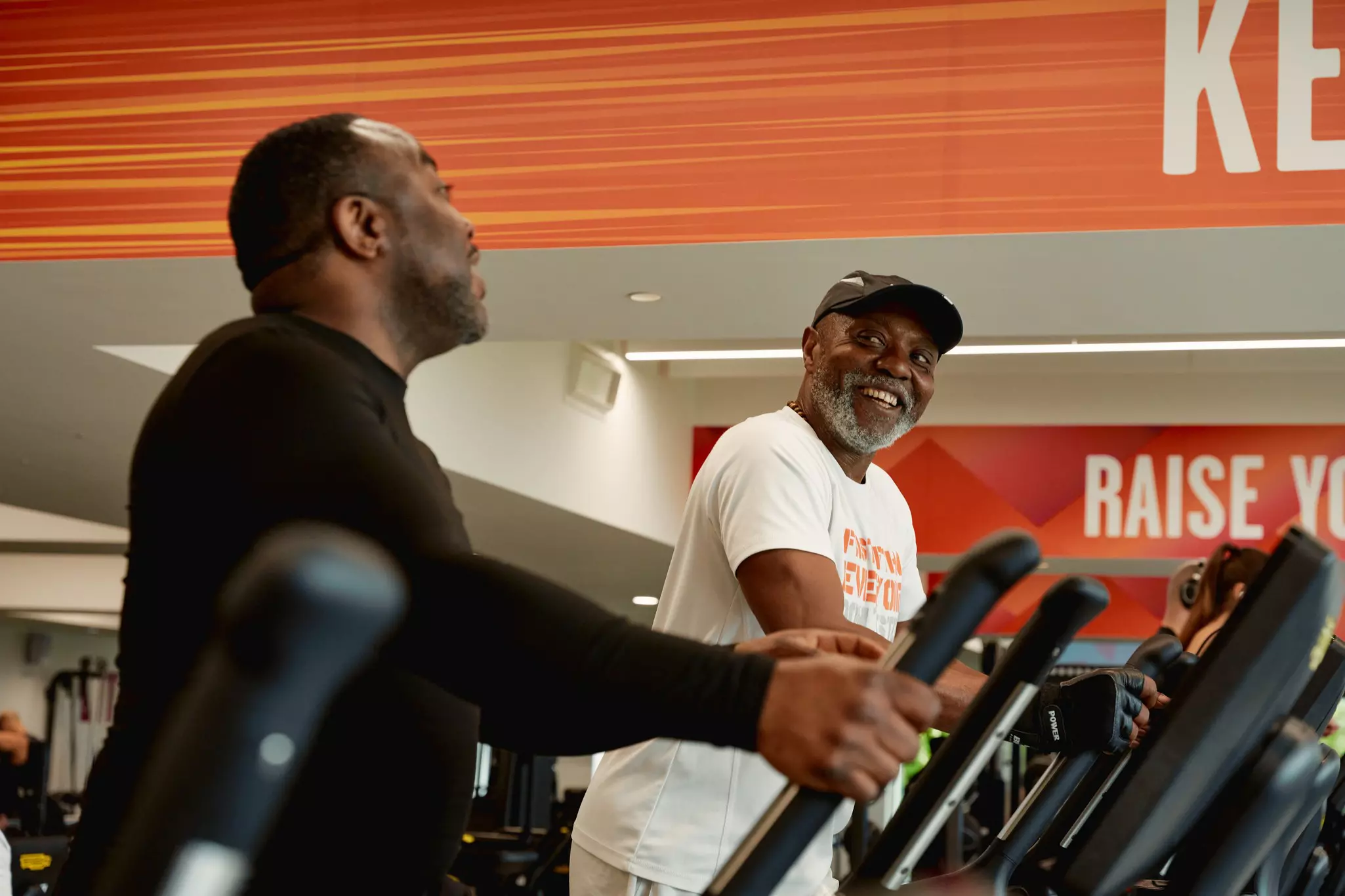 Two seniors chatting while on the treadmill in the gym.