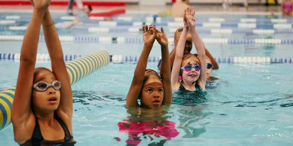 Children in a swimming lesson with arms raised in a pool.