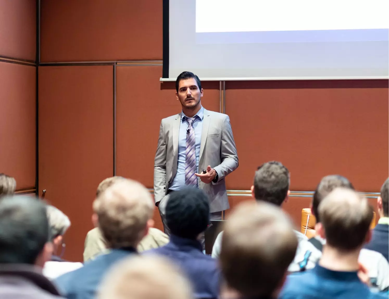 Man in a suit gives a presentation to a seated audience in a conference room.