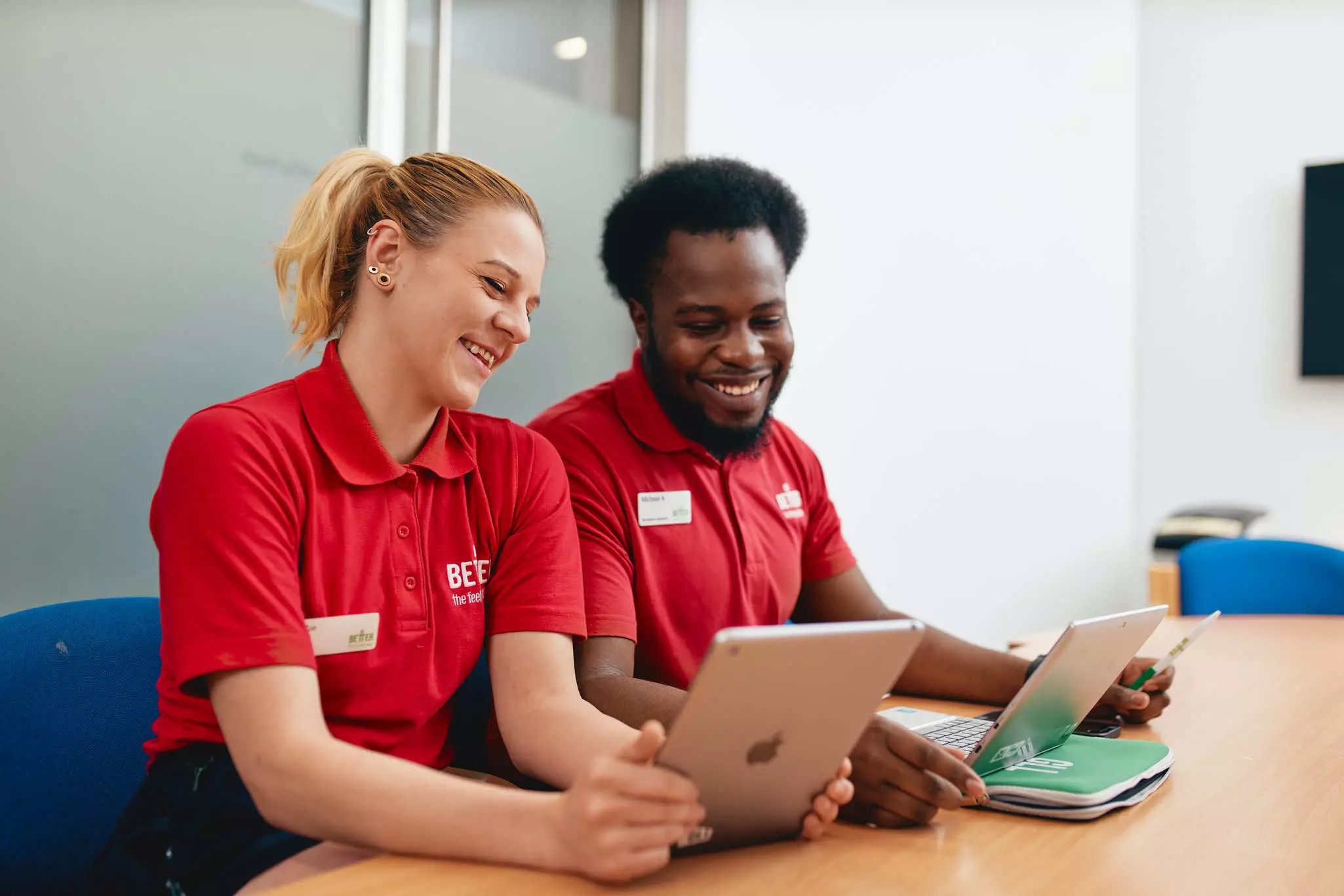 Two staff members in red uniforms using a tablet at a desk.