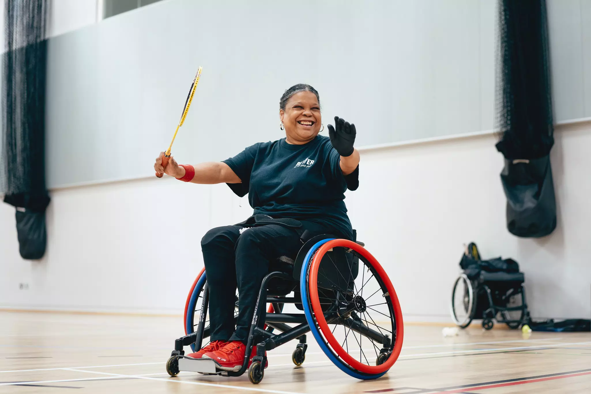 Person in wheelchair holding badminton racquet in a sports facility.