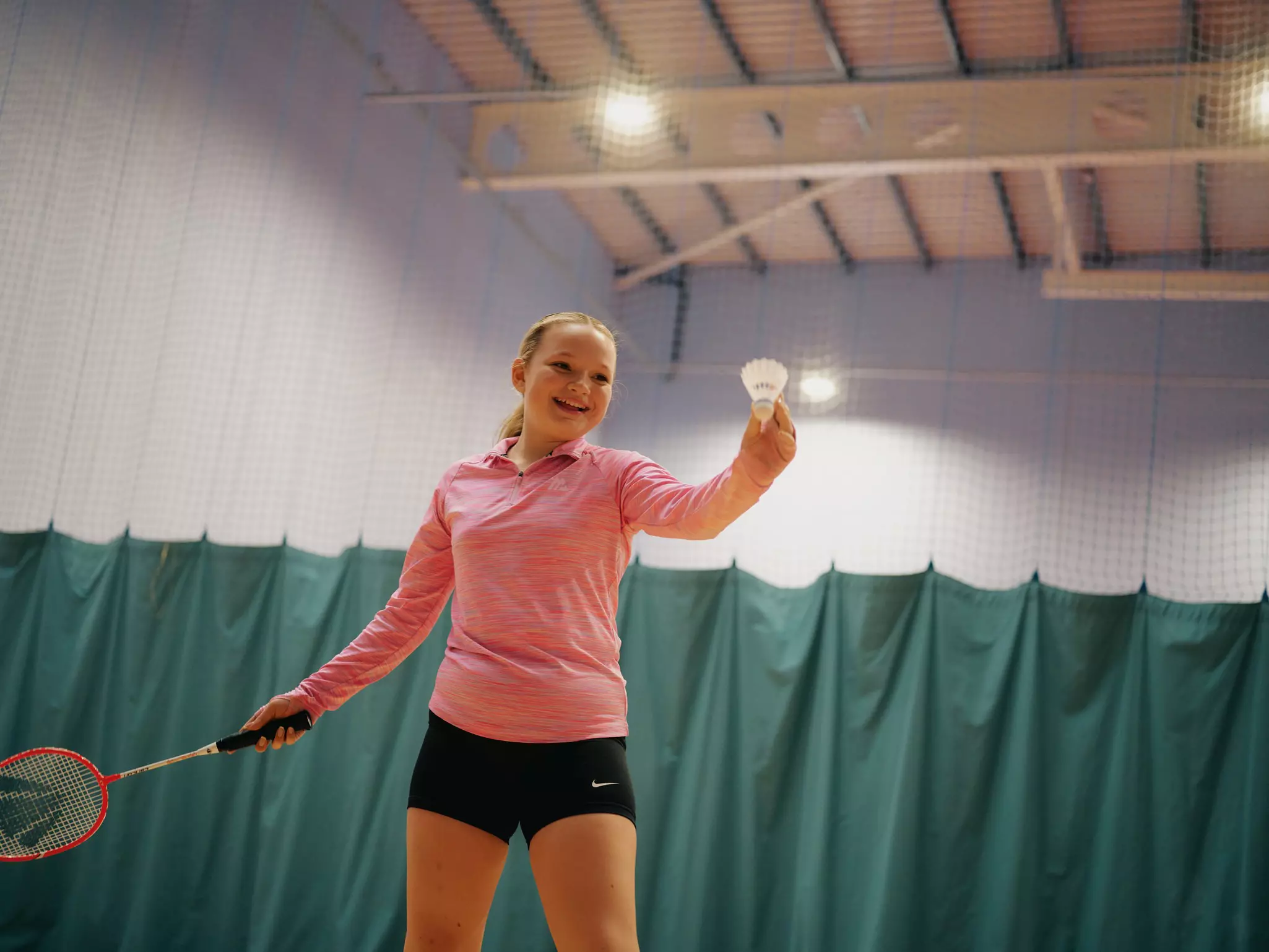 Child playing badminton in an indoor court with green dividers.