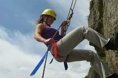Woman with yellow hard hat on abseiling down a wall