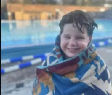Smiling child wrapped in a towel after swimming at an outdoor pool.