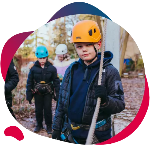 Boy wearing a helmet and harness holding a rope during an outdoor activity.