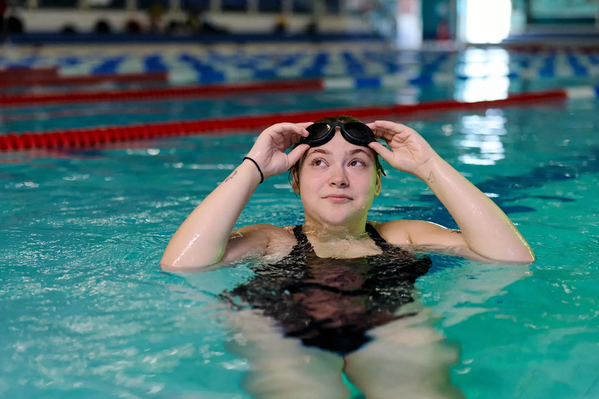 woman swimming in a pool with a green swimming cap on and goggles