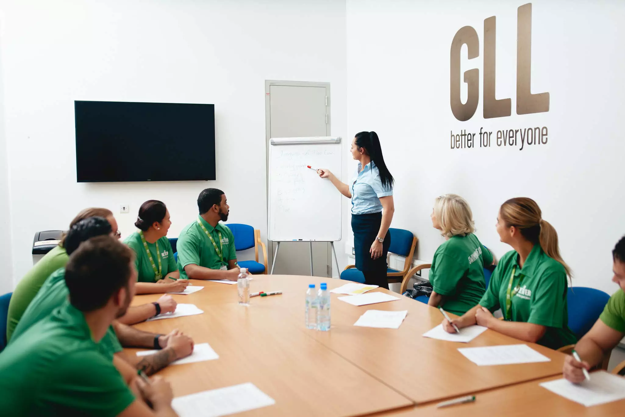 Team meeting with staff seated around a table and a presenter at the front.