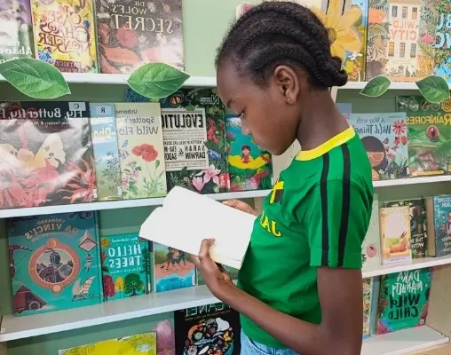 Child reads a book in front of a bookshelf.
