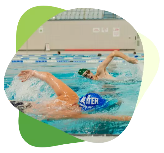 Two swimmers wearing caps and goggles doing front crawl in a lane of an indoor swimming pool.