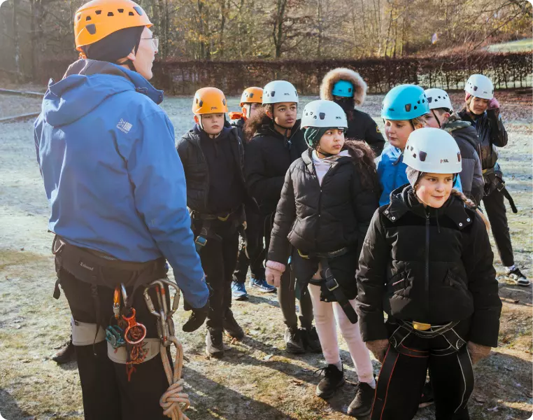 Group of children wearing helmets listening to an outdoor instructor.