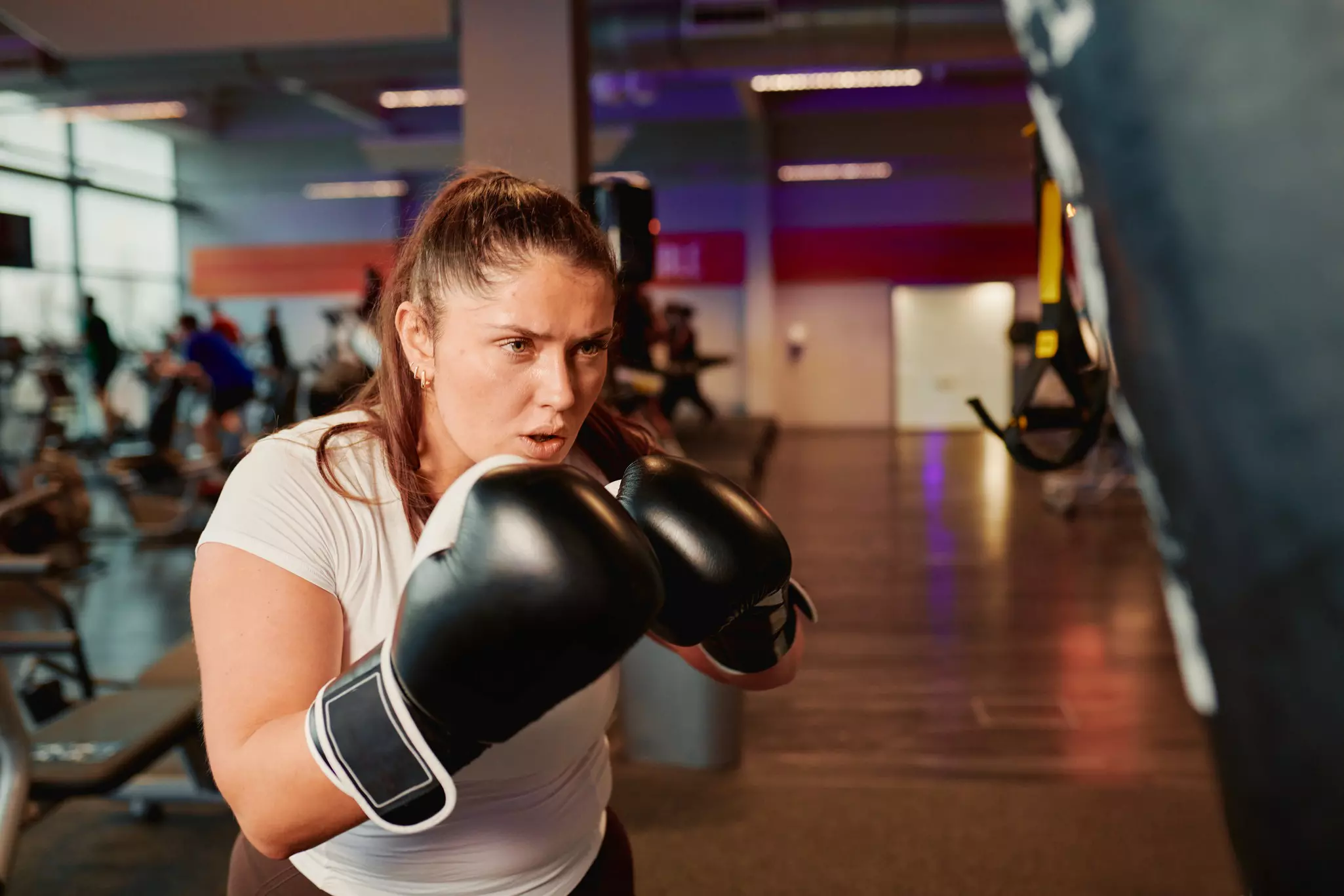 Person wearing boxing gloves and white tank top in a gym with purple lighting.