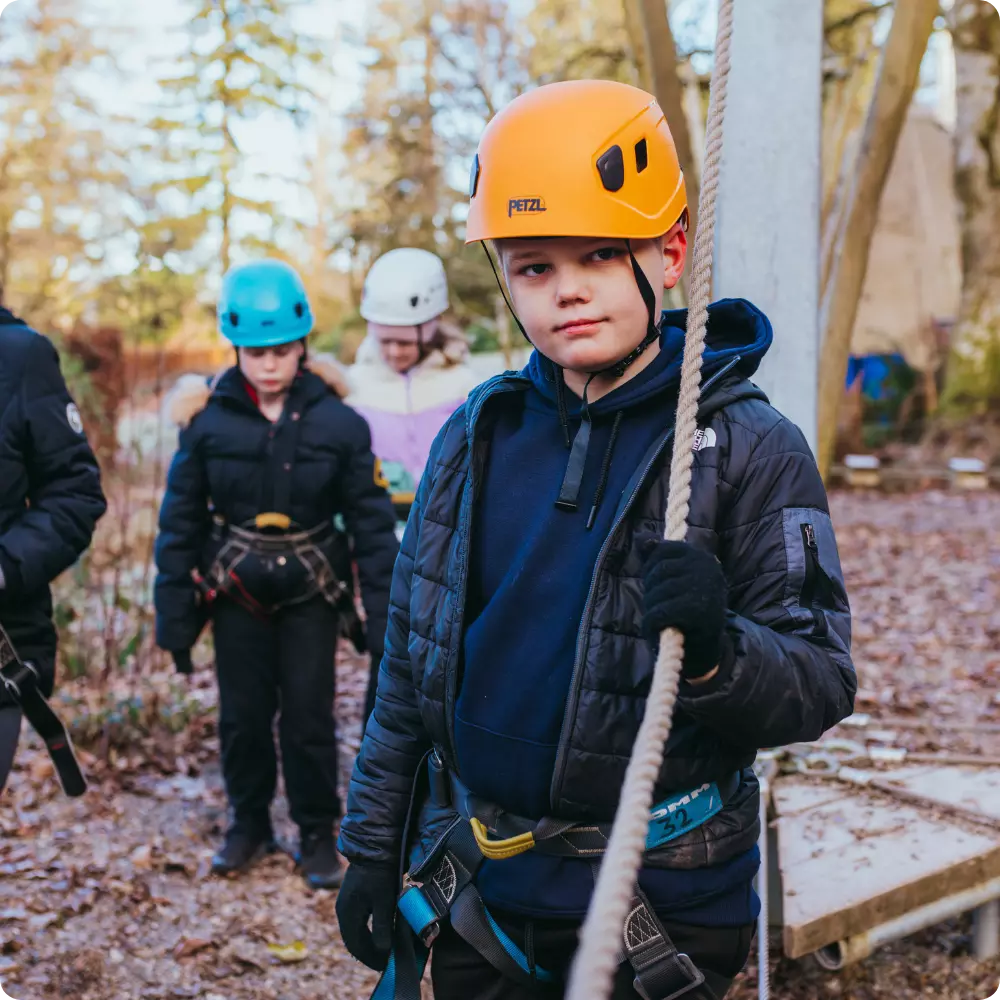 Boy wearing a helmet and harness holding a rope during an outdoor activity.
