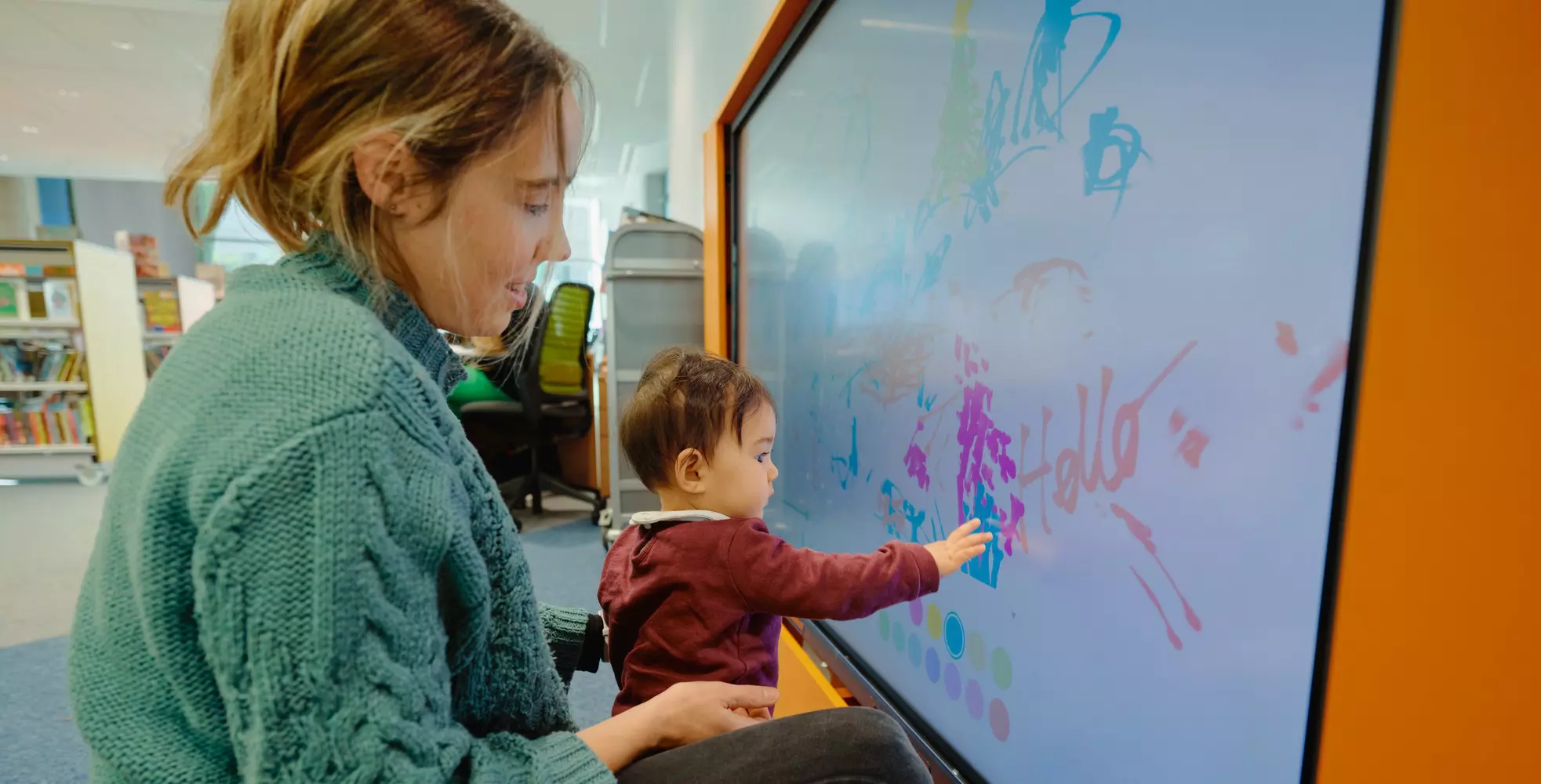 Child and adult drawing on a large interactive screen in a library.