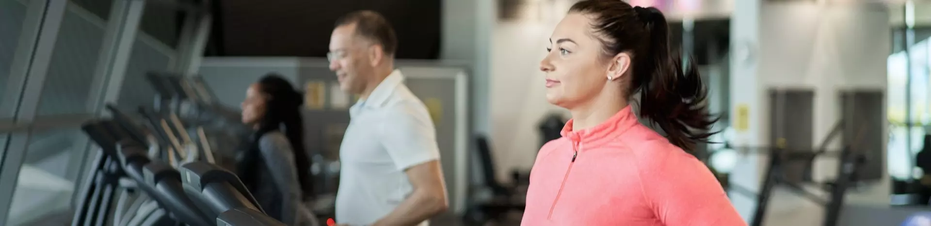 Woman in pink top running on treadmill with other gym members in background