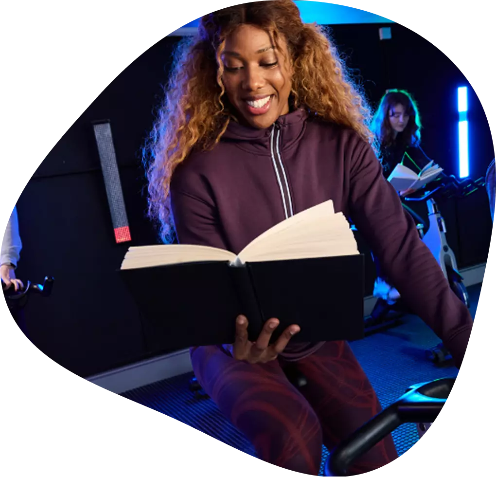 Woman on the indoor bike reading a book.
