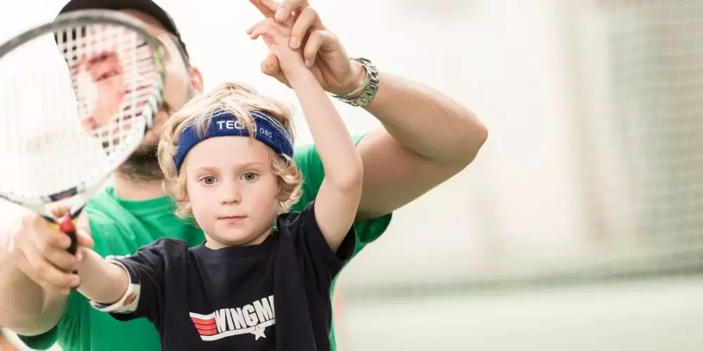 Child learning to play tennis with instructor guidance.