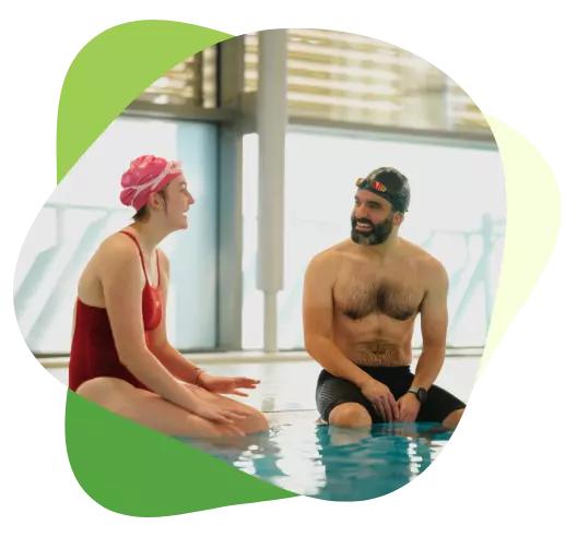 Two swimmers sitting at the edge of an indoor pool, smiling and chatting after a swim.