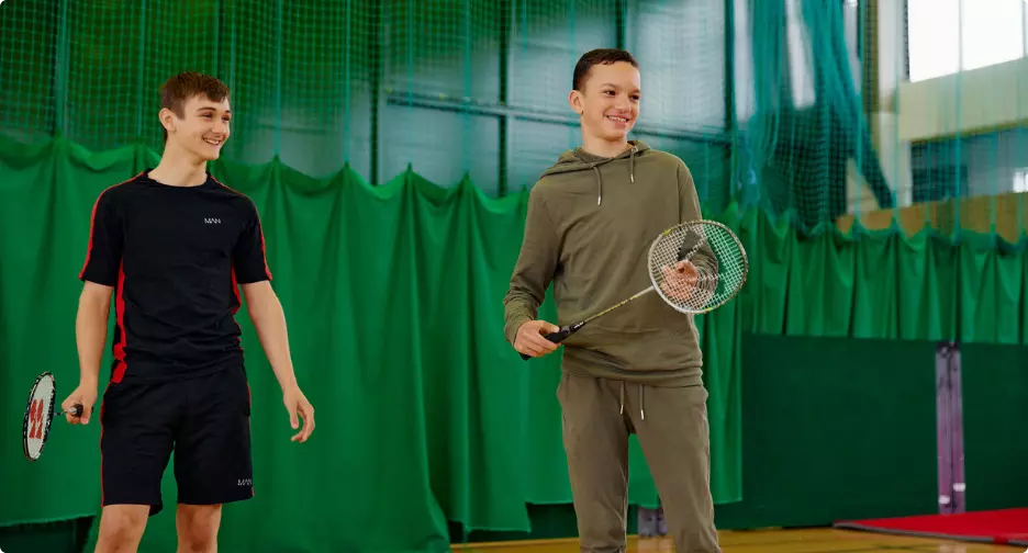 wo teenagers smiling with badminton rackets in a sports hall.