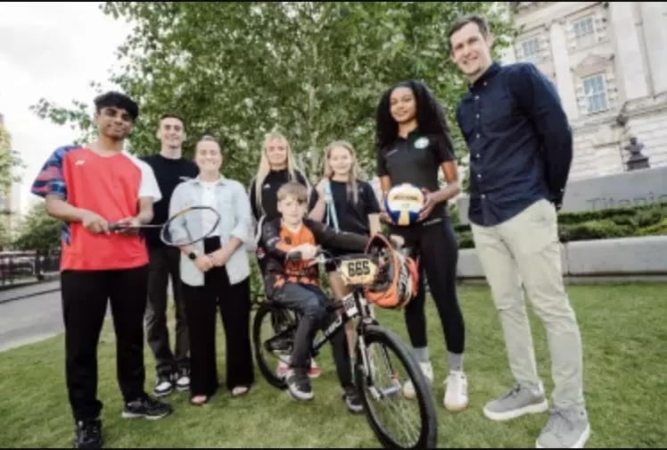 Group of young athletes posing with sports gear outside a civic building.