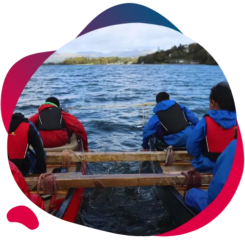 Children in waterproof gear paddling canoes on a lake.