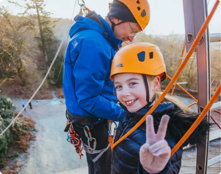 Smiling girl in a helmet giving a peace sign during a climbing activity.