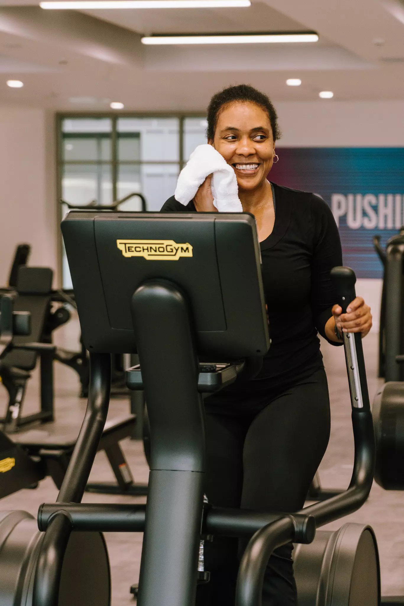 Woman on crosstrainer wiping her face with a towel