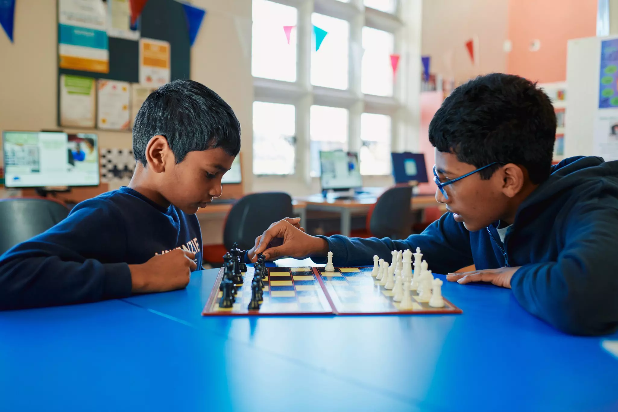Two boys focused on a chess match at a classroom table.