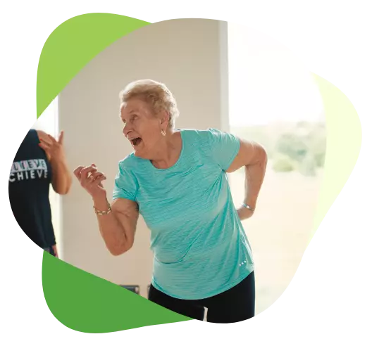 Smiling older woman dancing energetically in a bright indoor space during a fitness class.