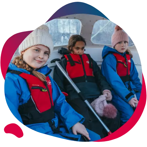 Three children in waterproof gear and life jackets sitting together in a boat.