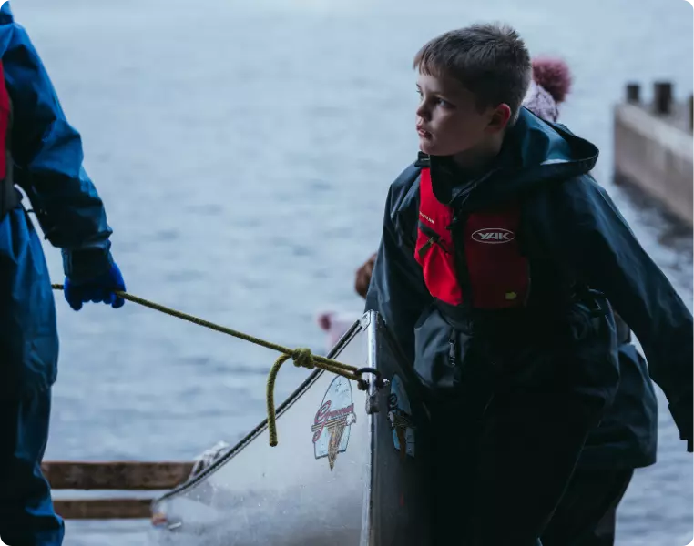 Boy in a life jacket helping to move a canoe by the water.