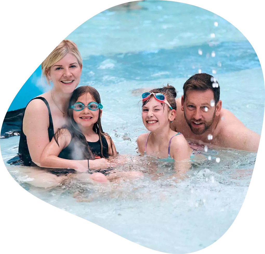 Family of four smiling together in a swimming pool.