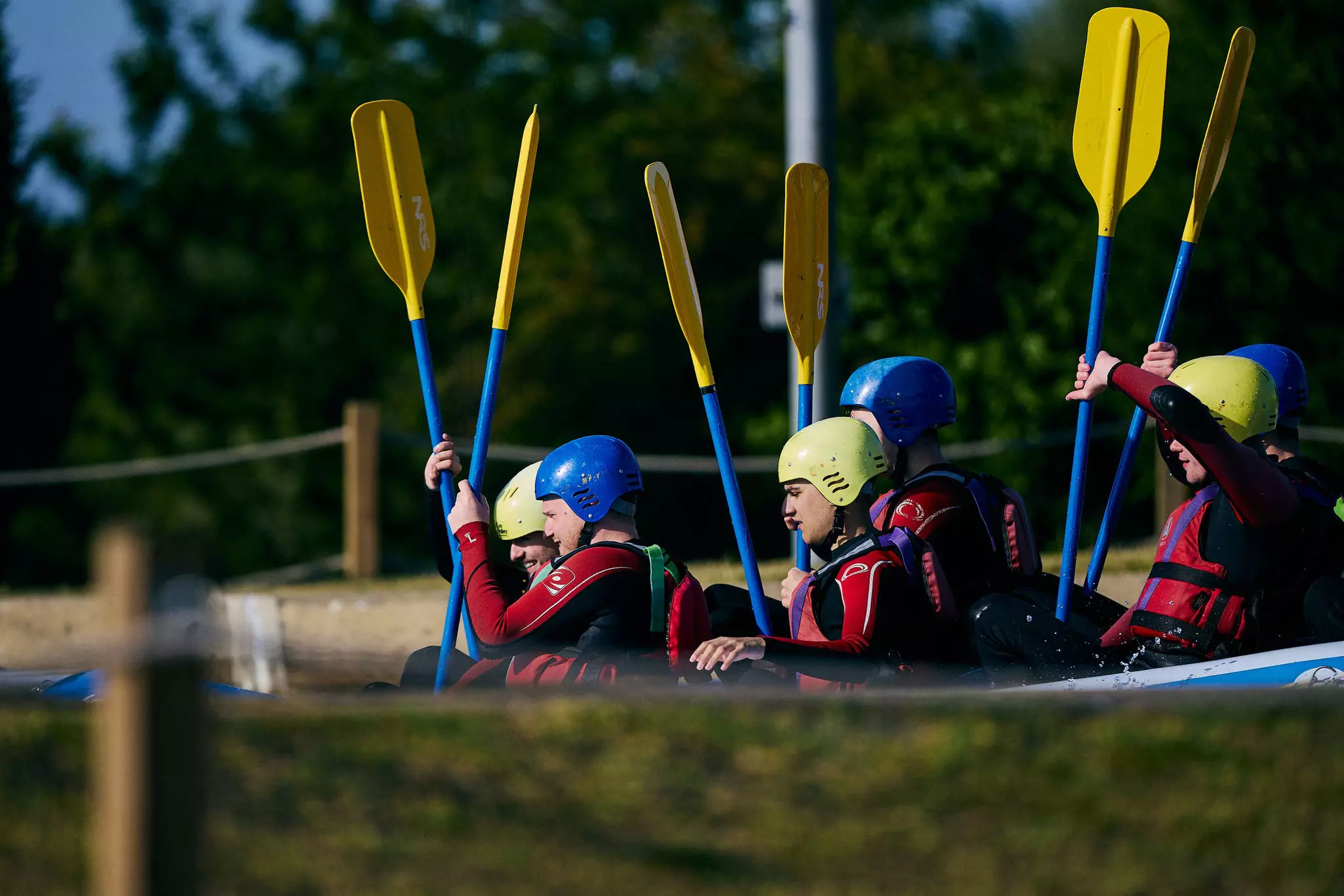 Group of people kayaking with paddles and wearing helmets and life jackets on water.