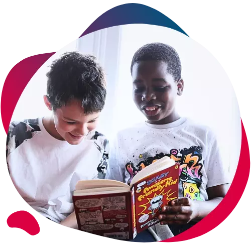 Two boys smiling while reading a book together.