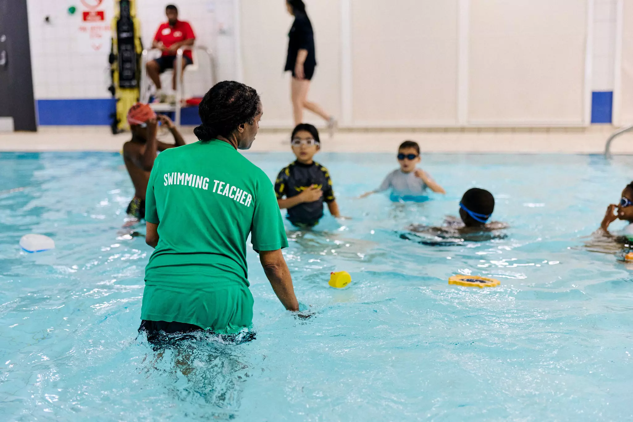 Swimming teacher instructing children in a pool with flotation aids.