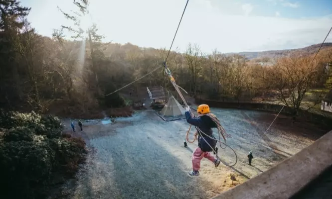 Girl in a helmet gripping a rope and swinging during an outdoor activity.