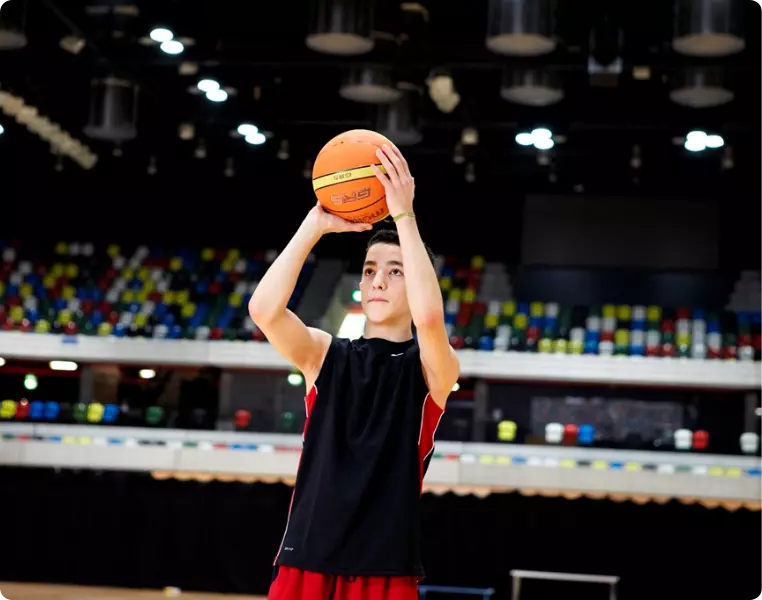 Young boy shooting a basketball in an indoor arena.