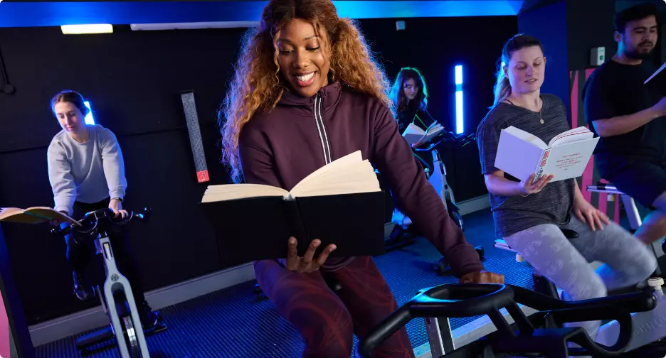 Group cycling class participants reading books while exercising.