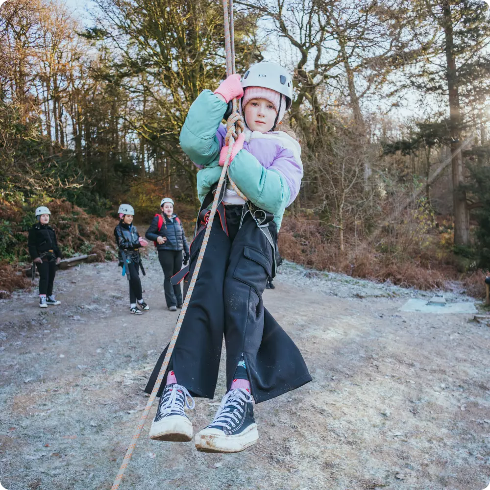 Girl in a helmet gripping a rope and swinging during an outdoor activity.