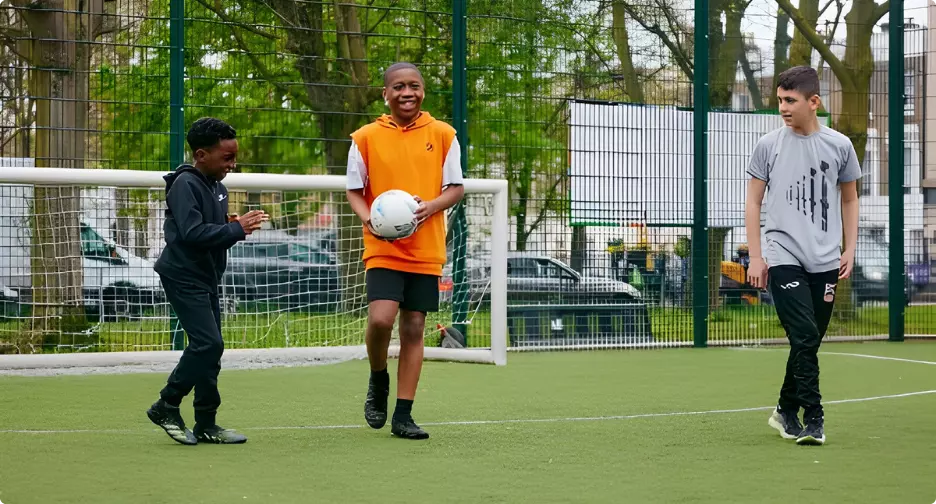 Three boys playing football on an outdoor pitch.